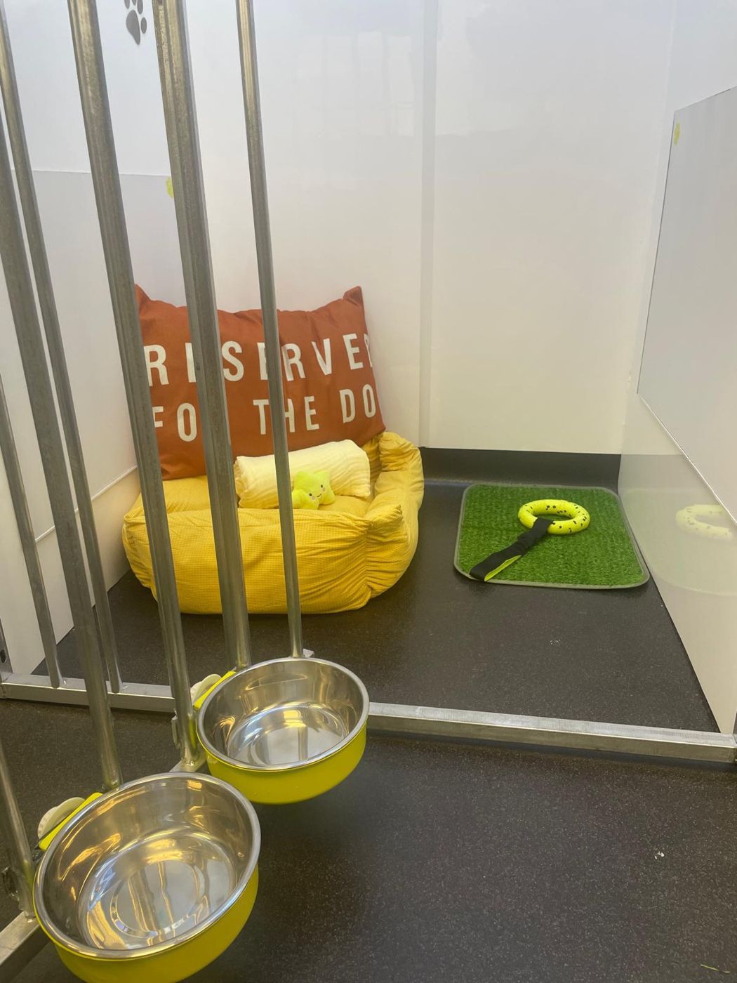 The yellow kennel with its gate open, showing the bed, grass patch and bowls